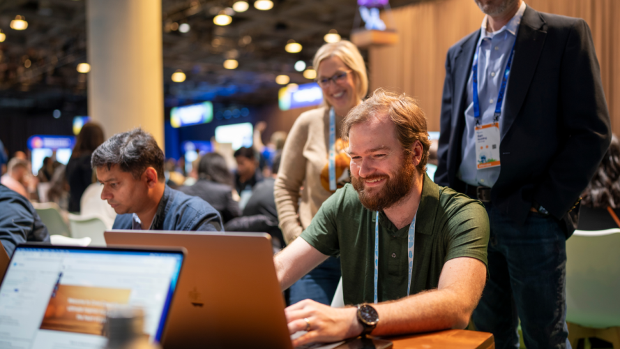 A man types on a laptop at Dreamforce while others look on.
