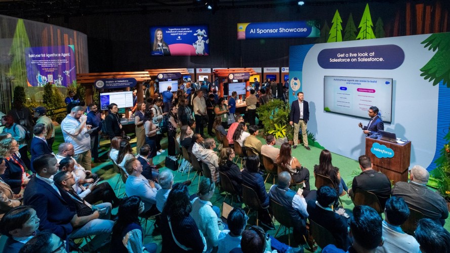 A group of attendees at Dreamforce 2024 sit in and watch two presenters deliver a Salesforce on Salesforce presentation