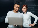 A team of two review Data Cloud and Salesforce Foundations on a computer in front of a black data screen.