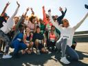 A diverse group of runners celebrates by taking a joyful selfie after completing a race. They're dressed in athletic wear with race numbers, capturing a moment of triumph and unity on a sunny day.