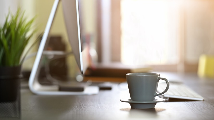 Morning light on desk computer and coffee cup.