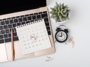 An aerial view of a computer calendar, pen, plant, and time clock to represent time blocking.