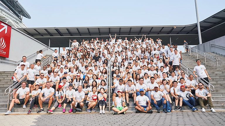 A large group of Salesforce Singapore employees dressed in white shirts pose together while sitting on the company's entrance steps.