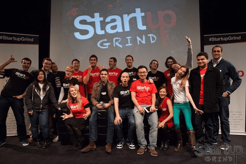 Alt Text: Group of enthusiastic attendees posing together on stage at a Startup Grind event.