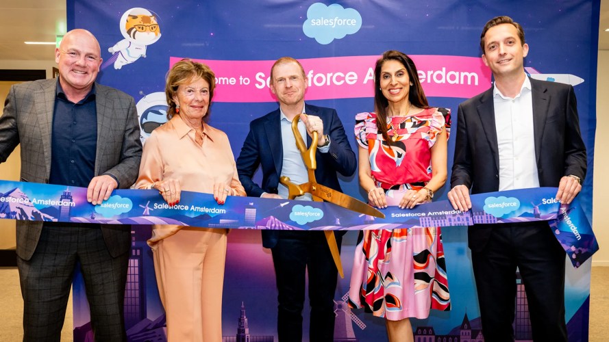 A group of five people is celebrating the opening of the Salesforce Amsterdam office with a ribbon-cutting ceremony.
