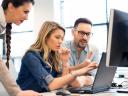 Three employees working on a computer to train on software.