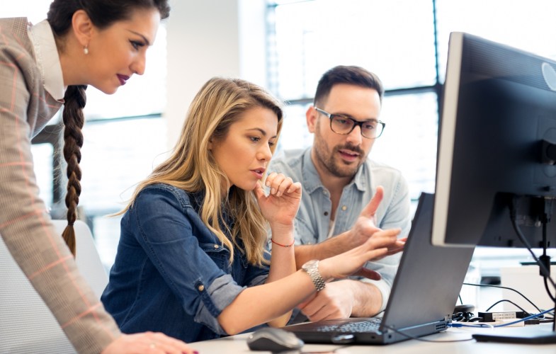 Three employees working on a computer to train on software.
