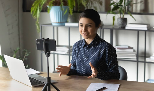 A SMB owner making a video at a desk with a smartphone, tripod and computer.