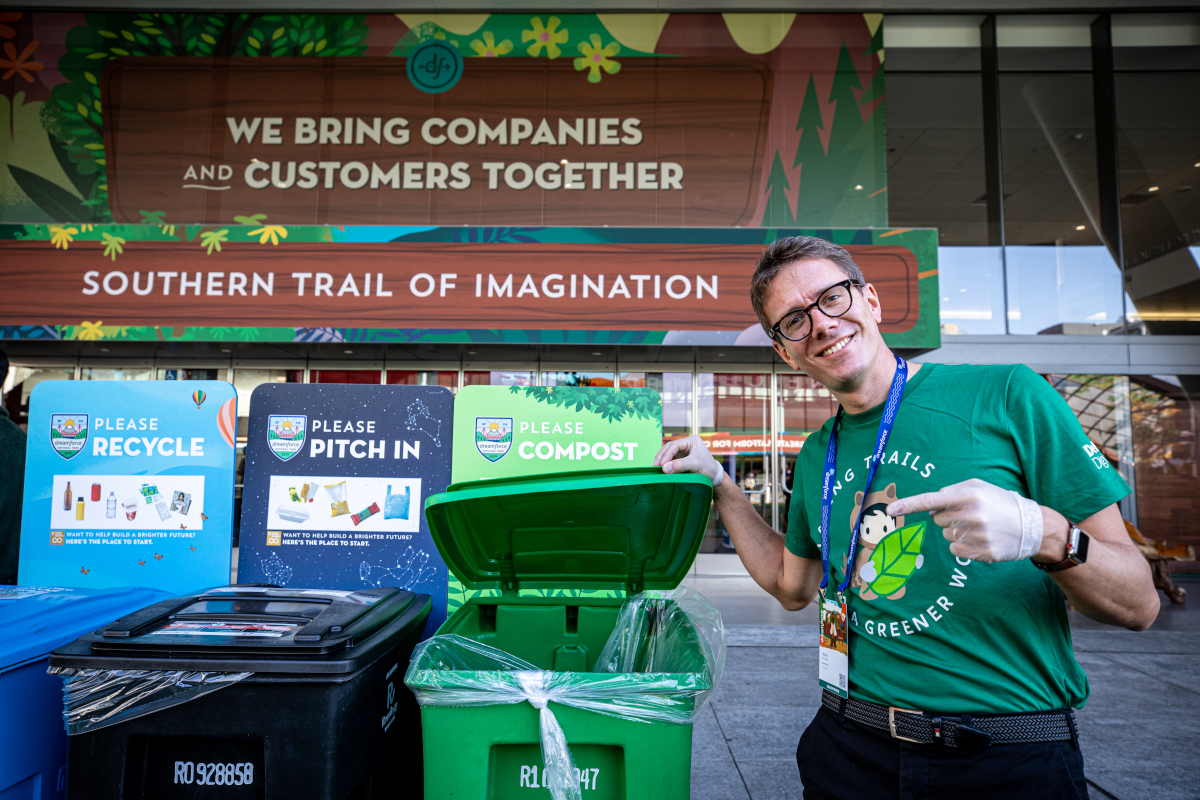 A Salesforce volunteer poses in front of compost, recycling, and trash bins at Dreamforce.