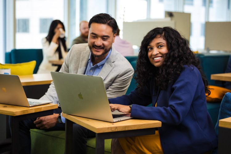 Two employees sitting in a modern office space work together at a computer
