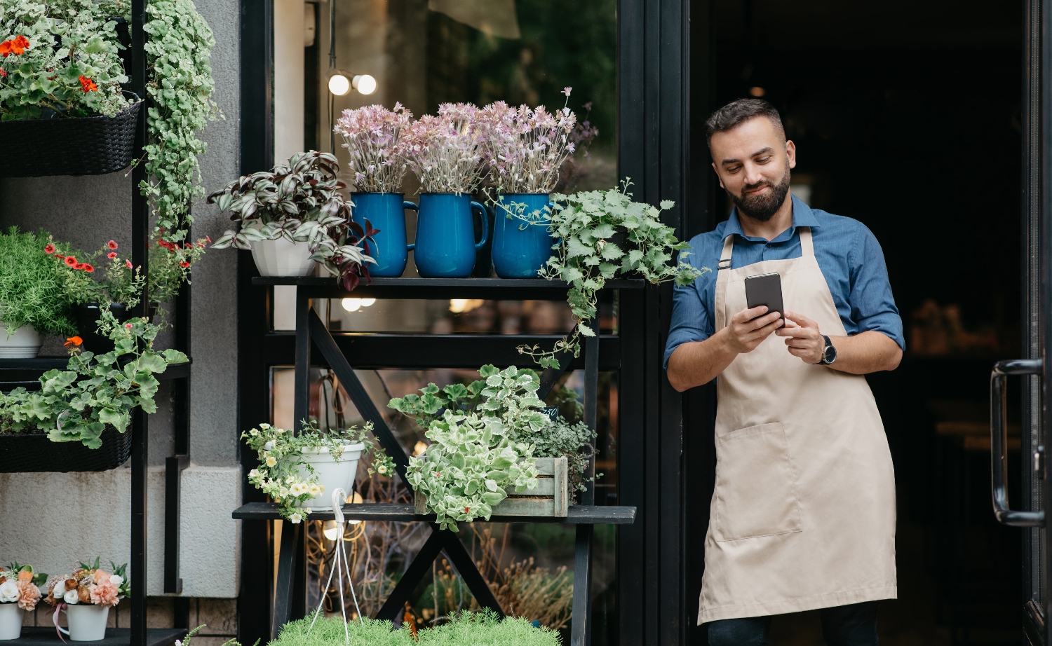A flower shop small business owner leaning in the doorway looking at phone, suggesting supporting a small business.