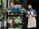 A flower shop small business owner leaning in the doorway looking at phone, suggesting supporting a small business.