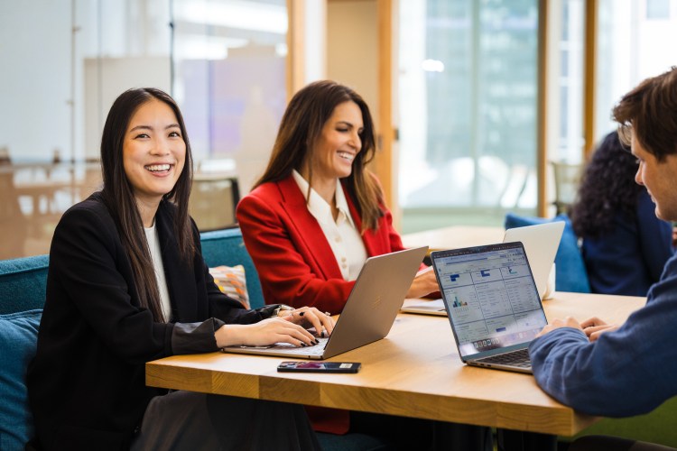 group of three employees sit in a modern office space and work on their computers