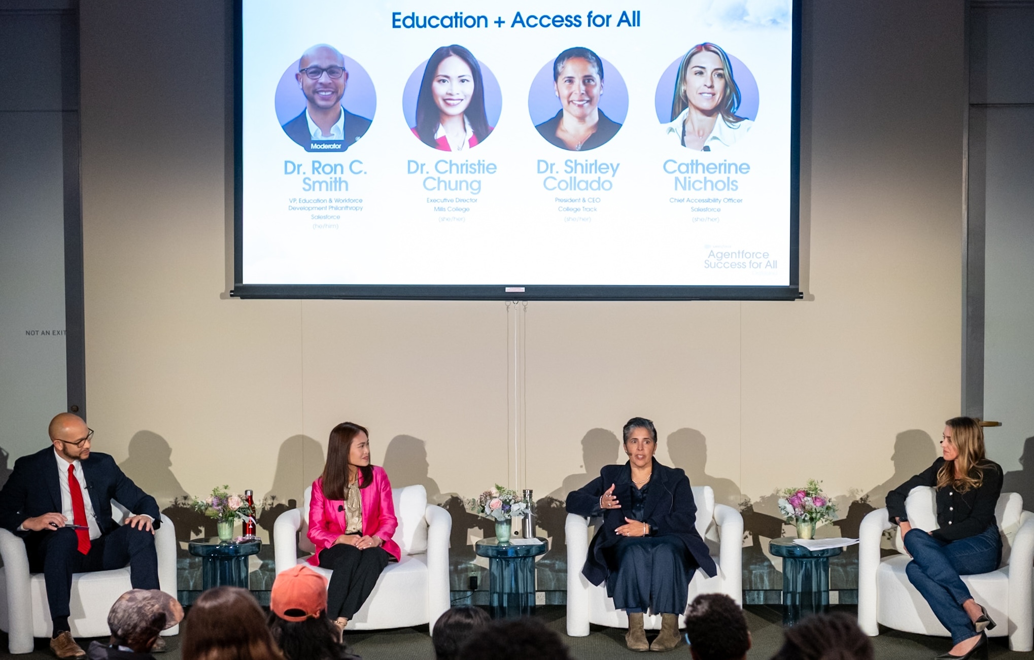 Onstage and seated in white club chairs, Dr. Ron Smith in a black suit and red tie, Dr. Christie Chung in a pink jacket and black pants, Dr. Shirley Collado in navy dress and jacket, and Catherine Nichols in navy sweater and pants. Between each pair, a translucent blue round table with pink, white, and green florals. Behind them, a cream wall with a large screen that shows "Education and Access for All" with each speaker's headshot, name, and title.