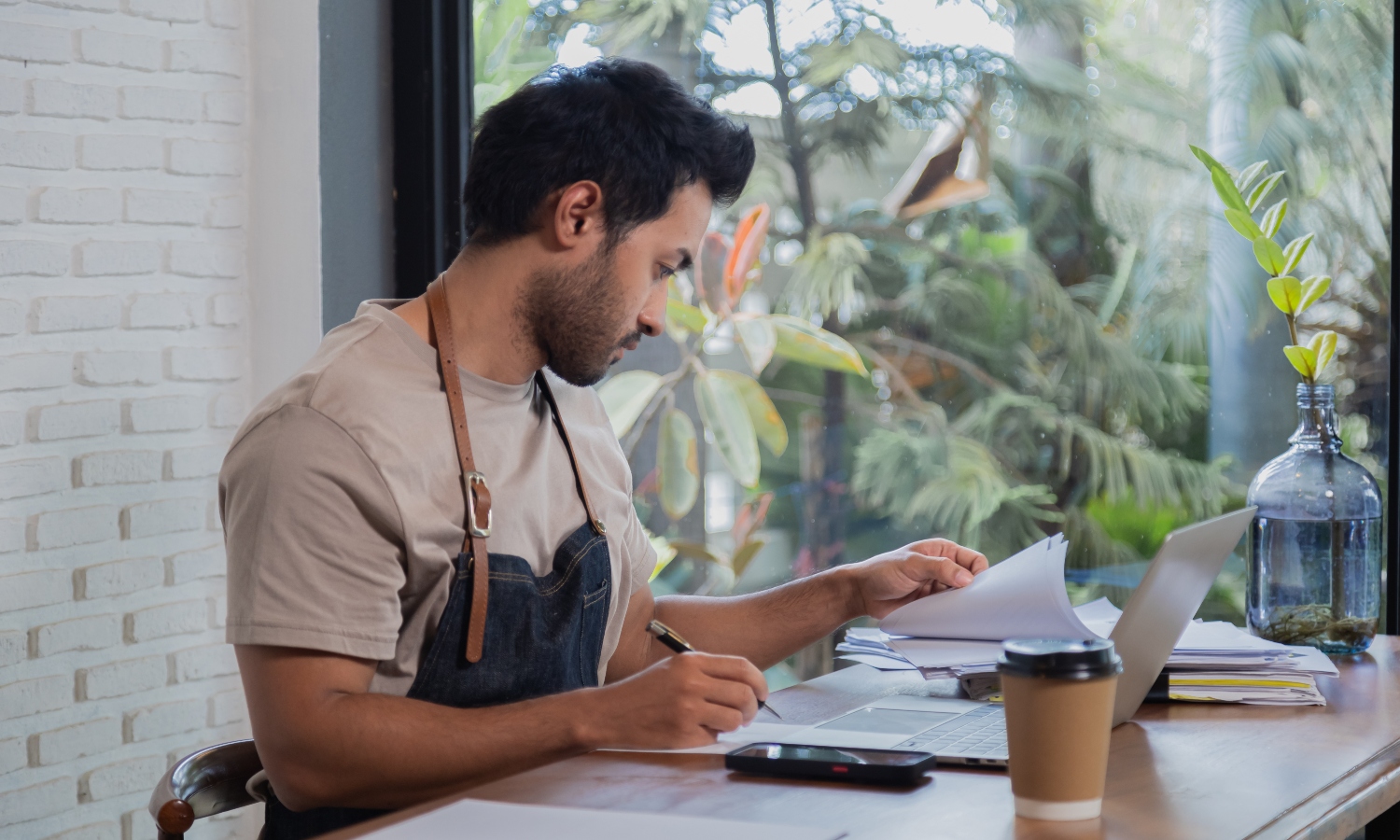 Attractive barista male or employee concentrate on stacks of tax declaration bills, restaurant owner using laptop for bookkeeping control payment, multitask small business lifestyle doing everything