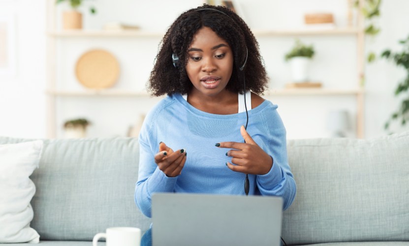 A customer service representative using free courses on a laptop at home on a headset.
