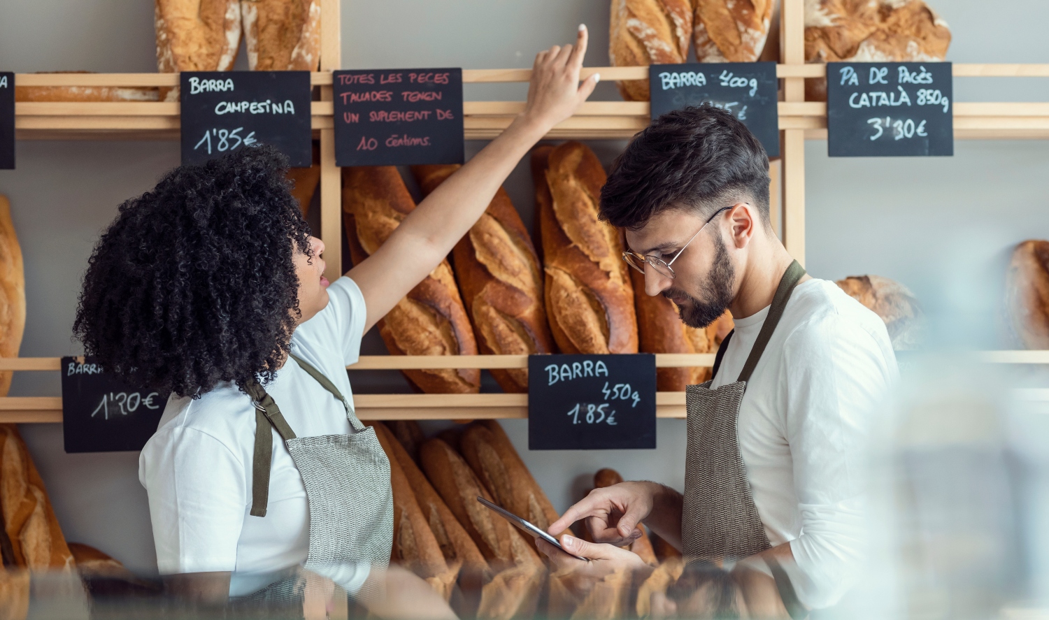 Two local bakery owners reviewing a data driven marketing strategy pointing at their bread at the counter, calculating.