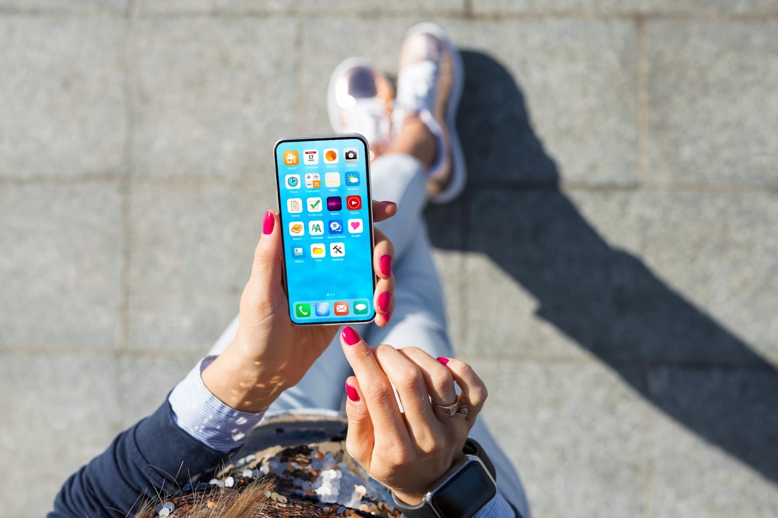 A POV shot looking down at a phone being held by two hands with red finger nails, and the user is sitting down.
