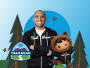 A male Trailblazer and Salesforce character Astro in black hoodies showcasing Trailhead and forest on a blue background.