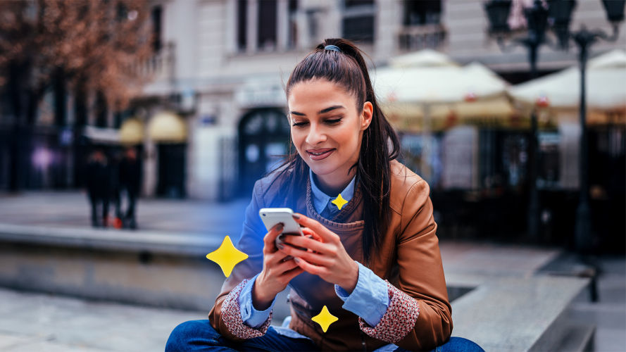 Person sitting outside that is smiling while looking at their phone. The phone has three yellow stars around it.