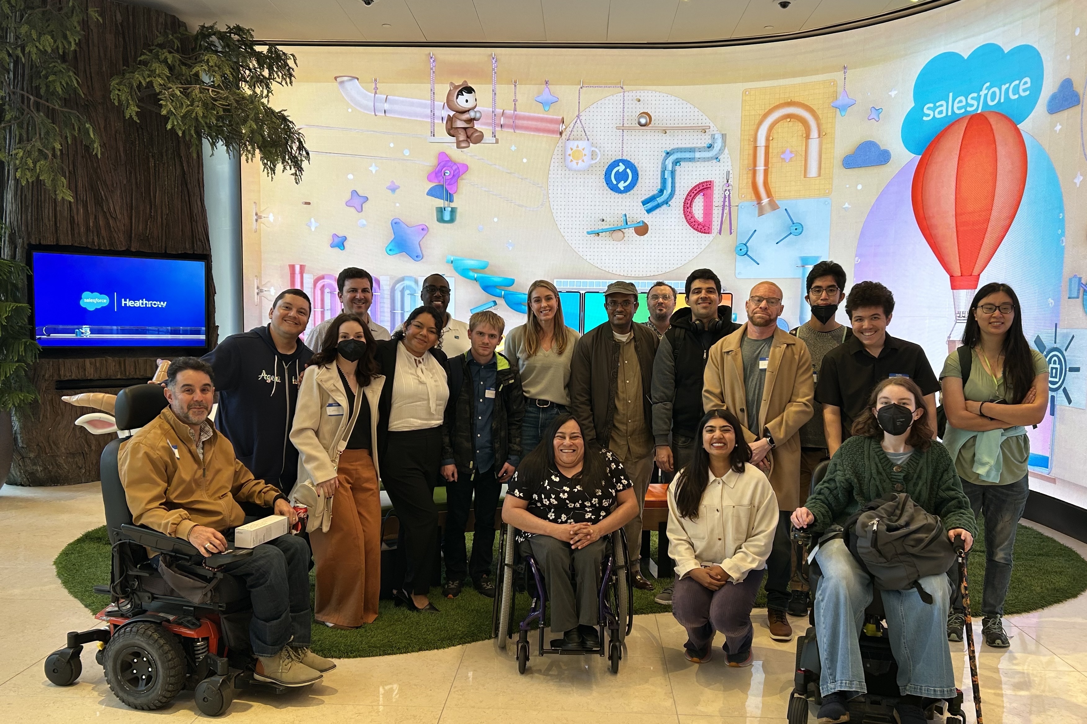 Members from the Center for Independent Living with Workforce Navigators Analyst, Lucia Rios, during a visit to Salesforce Tower in San Francisco. Behind them, a digital screen with Salesforce characters and the cloud logo.