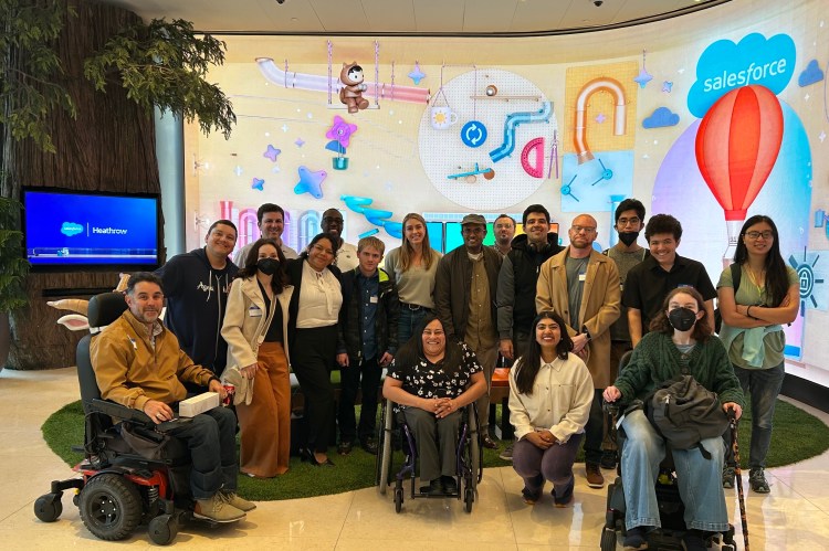 Members from the Center for Independent Living with Workforce Navigators Analyst, Lucia Rios, during a visit to Salesforce Tower in San Francisco. Behind them, a digital screen with Salesforce characters and the cloud logo.