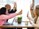 four employees high five over a table in a modern office space