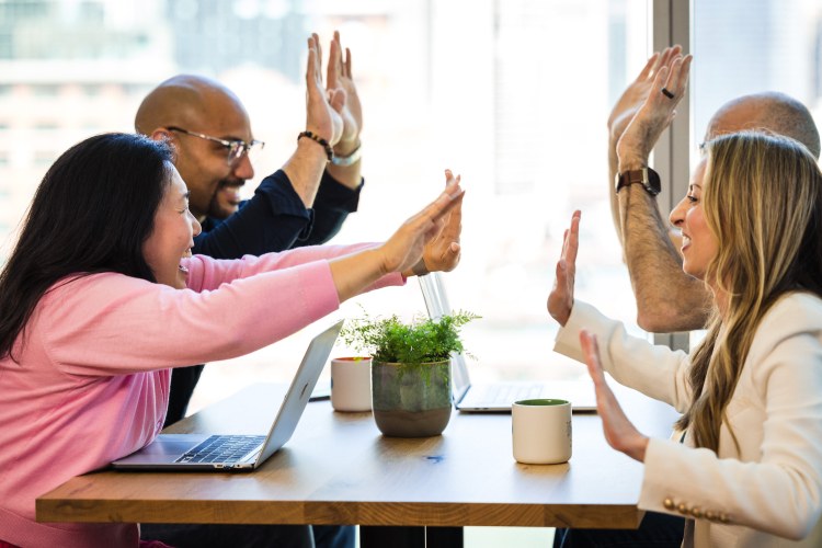 four employees high five over a table in a modern office space