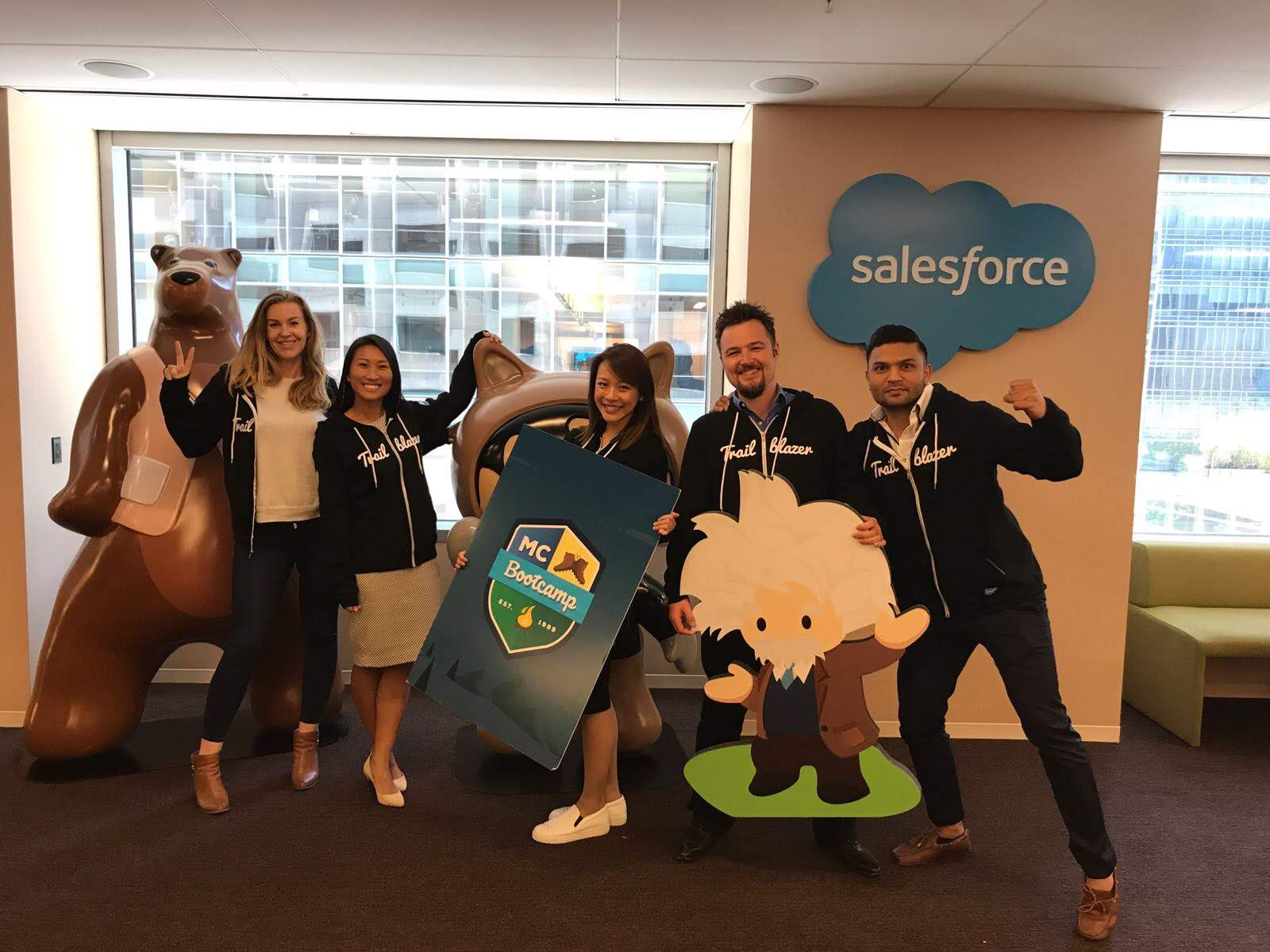 five employees pose in a modern office space and smile for the camera