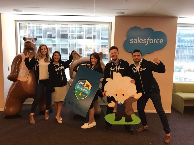 five employees pose in a modern office space and smile for the camera