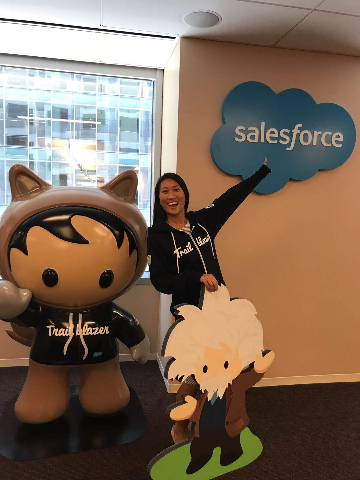 woman stands in modern office space and poses with salesforce mascots