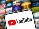 A YouTube icon on a smart phone with a showcase of television screens showing media behind it.