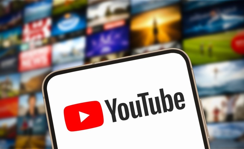 A YouTube icon on a smart phone with a showcase of television screens showing media behind it.
