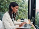 Earphones, laptop and remote work with woman at window in home for online planning or leading a team asynchronously.