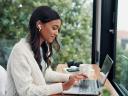 Earphones, laptop and remote work with woman at window in home for online planning or leading a team asynchronously.