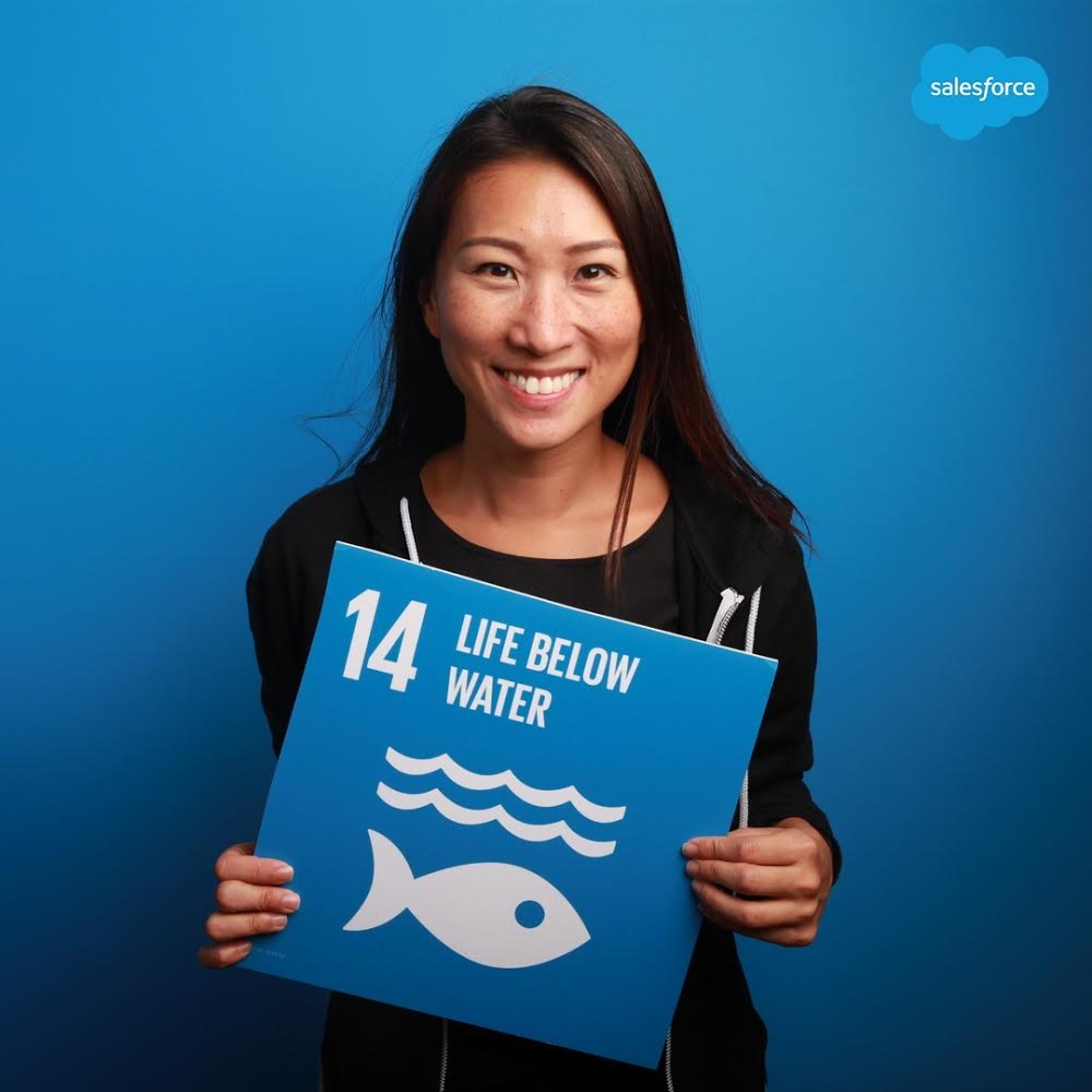 woman stands against a blue background holding a sign that says "life below water"