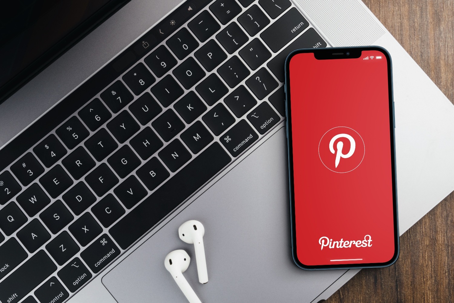 Pinterest app on the smartphone screen on wooden background with a computer beside it