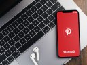 Pinterest app on the smartphone screen on wooden background with a computer beside it