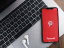 Pinterest app on the smartphone screen on wooden background with a computer beside it