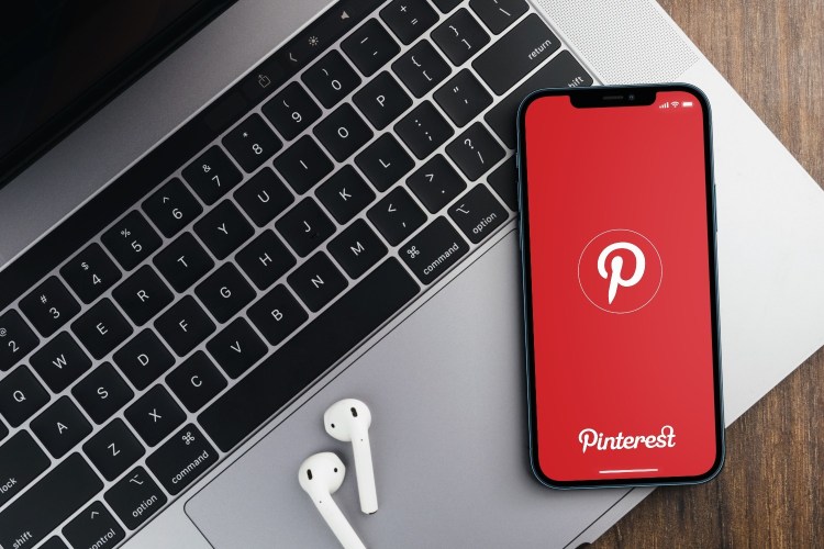 Pinterest app on the smartphone screen on wooden background with a computer beside it