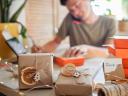 Young millennial worker packing Christmas gift boxes for clients, family small business.
