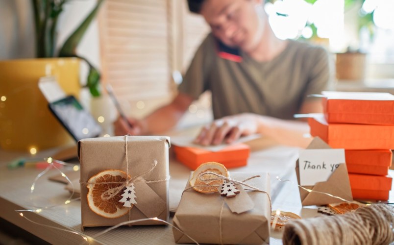 Young millennial worker packing Christmas gift boxes for clients, family small business.