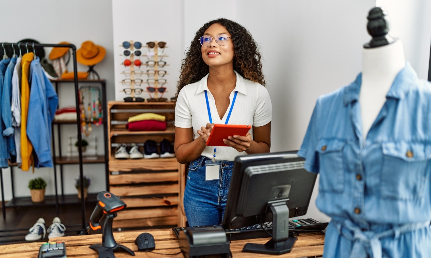 Young latin shopkeeper woman using touchpad working at clothing store.