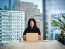 A woman sits in a modern office space in front of a computer