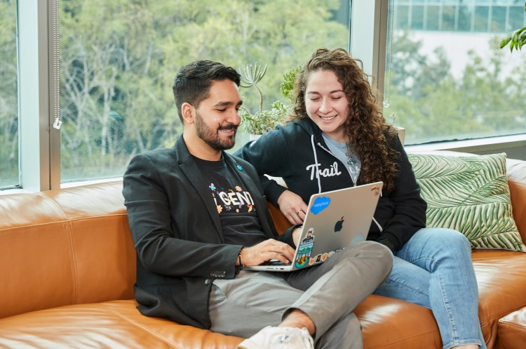 man and woman sit in a modern office space and collaborate over a laptop