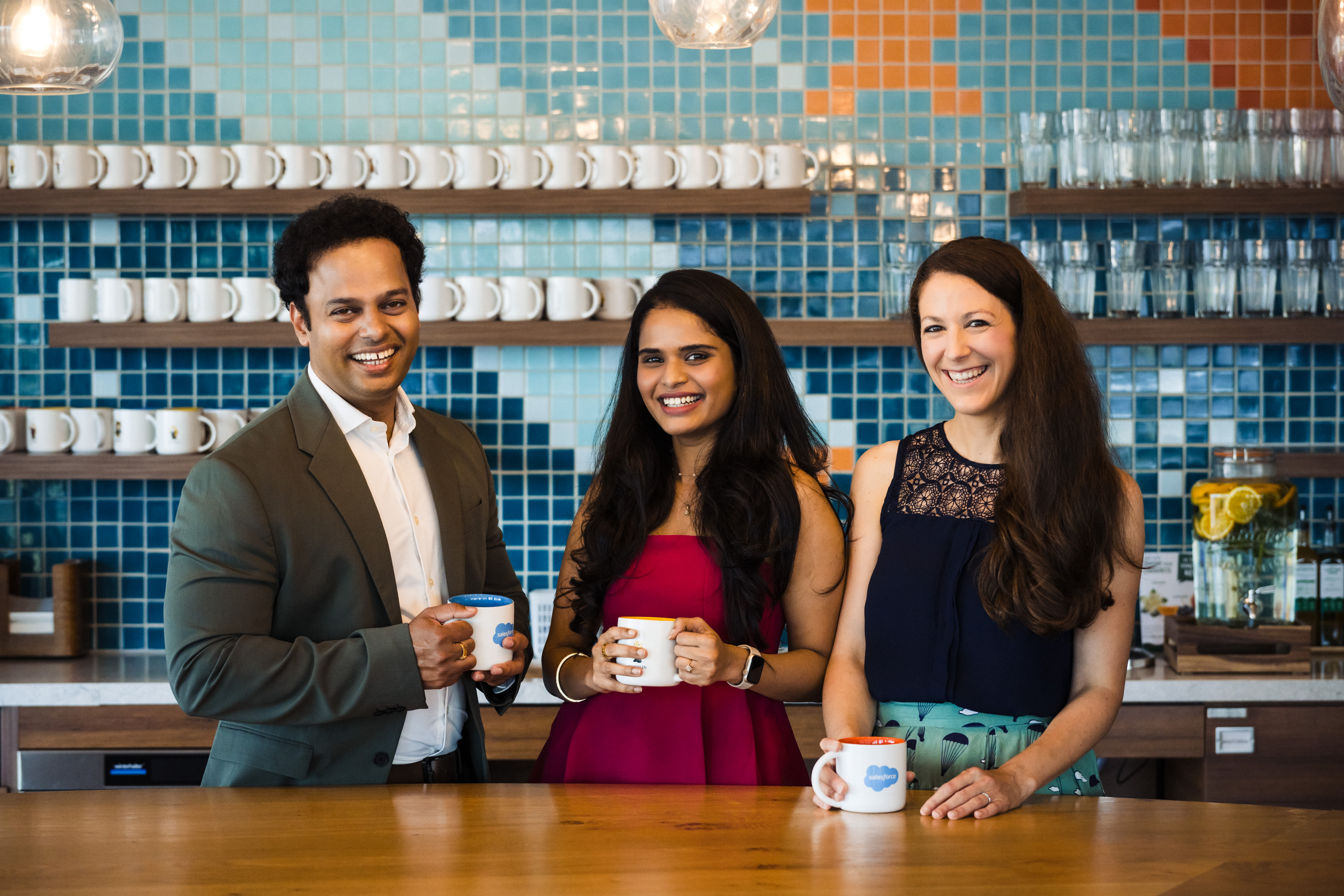 group of three employees pose together in the kitchen of a modern office space