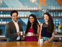 group of three employees pose together in the kitchen of a modern office space