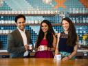 group of three employees pose together in the kitchen of a modern office space