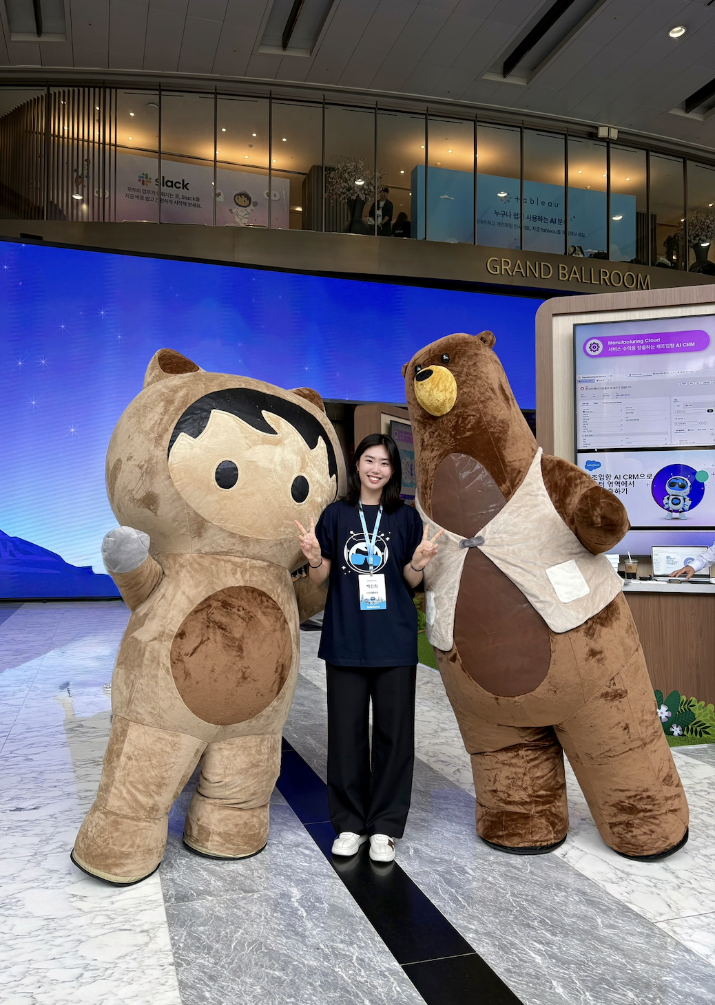 woman stands in a ballroom-style room with two life-sized salesforce mascots