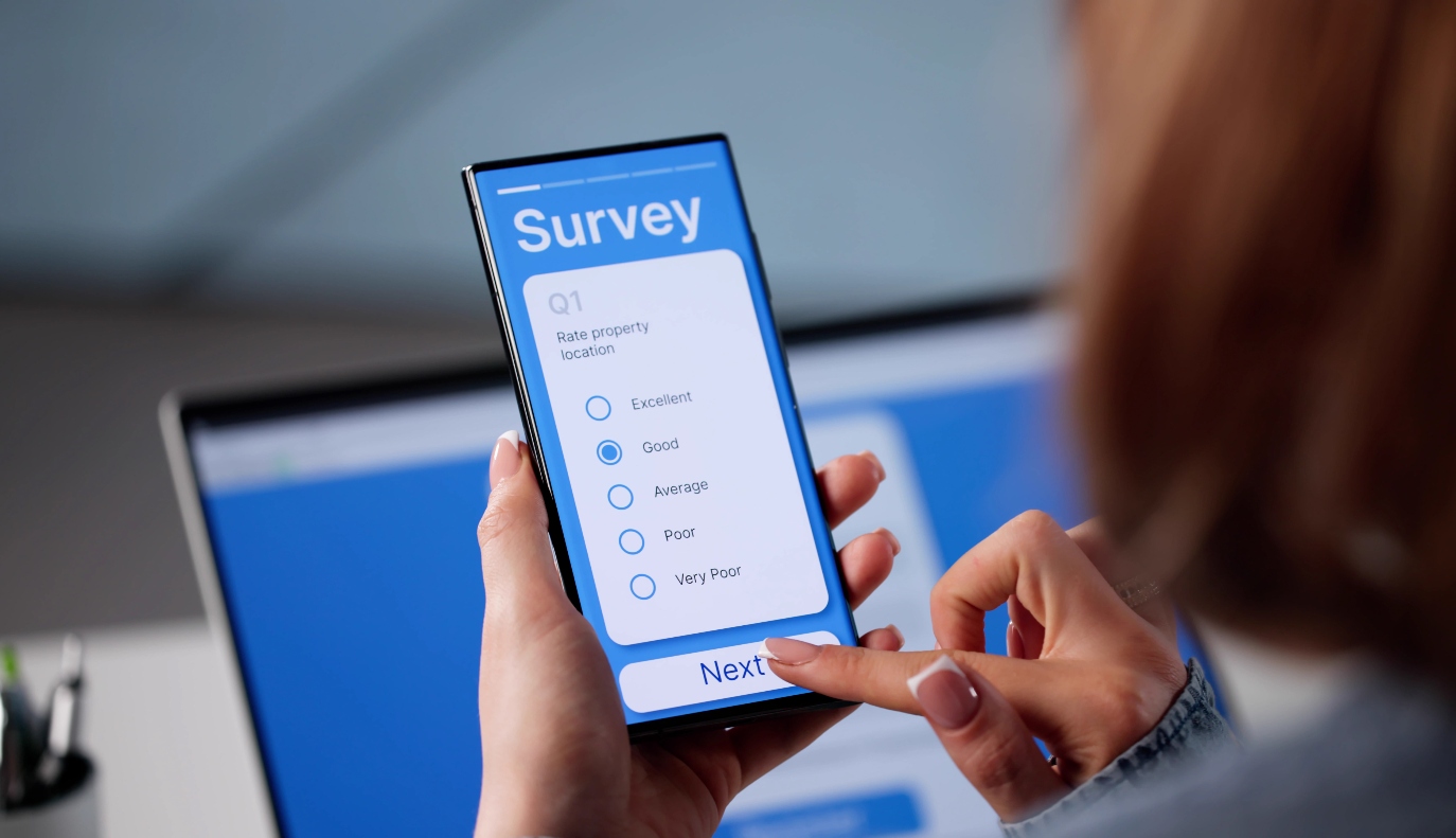 A business woman sitting at a desk filling out a survey on mobile in an office setting.